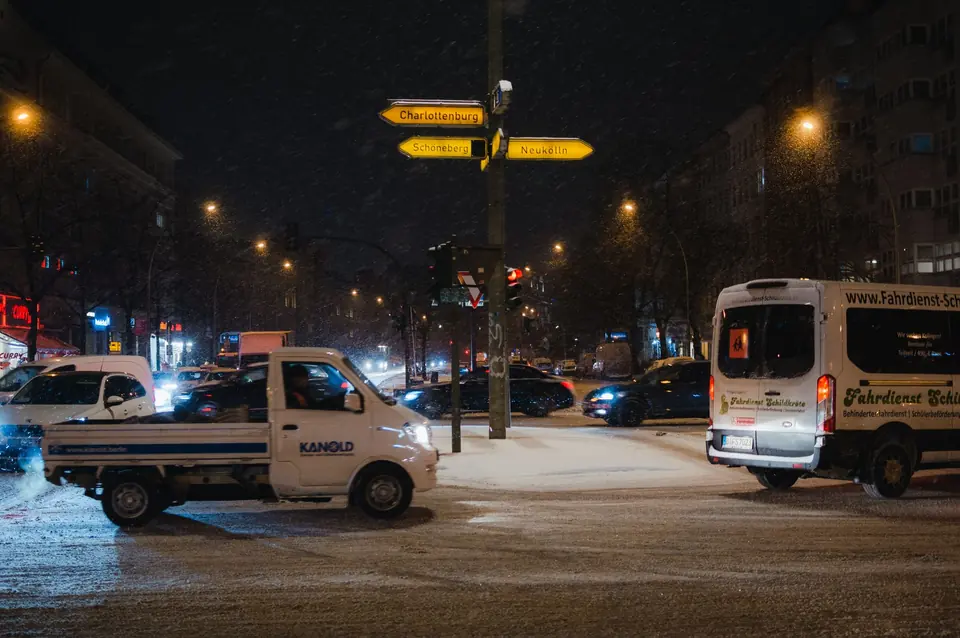 Schneefall an einer belebten Berliner Kreuzung in der Nacht mit gut sichtbaren Schildern. Städtische Winterszene.